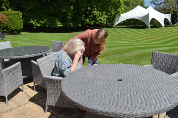 lady sitting feeling ill with a standing female looking concerned in a garden